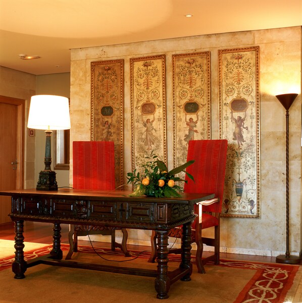 Una habitación con una mesa de madera, sillas rojas, un tapete rojo y una pared con motivos florales ornamentados.