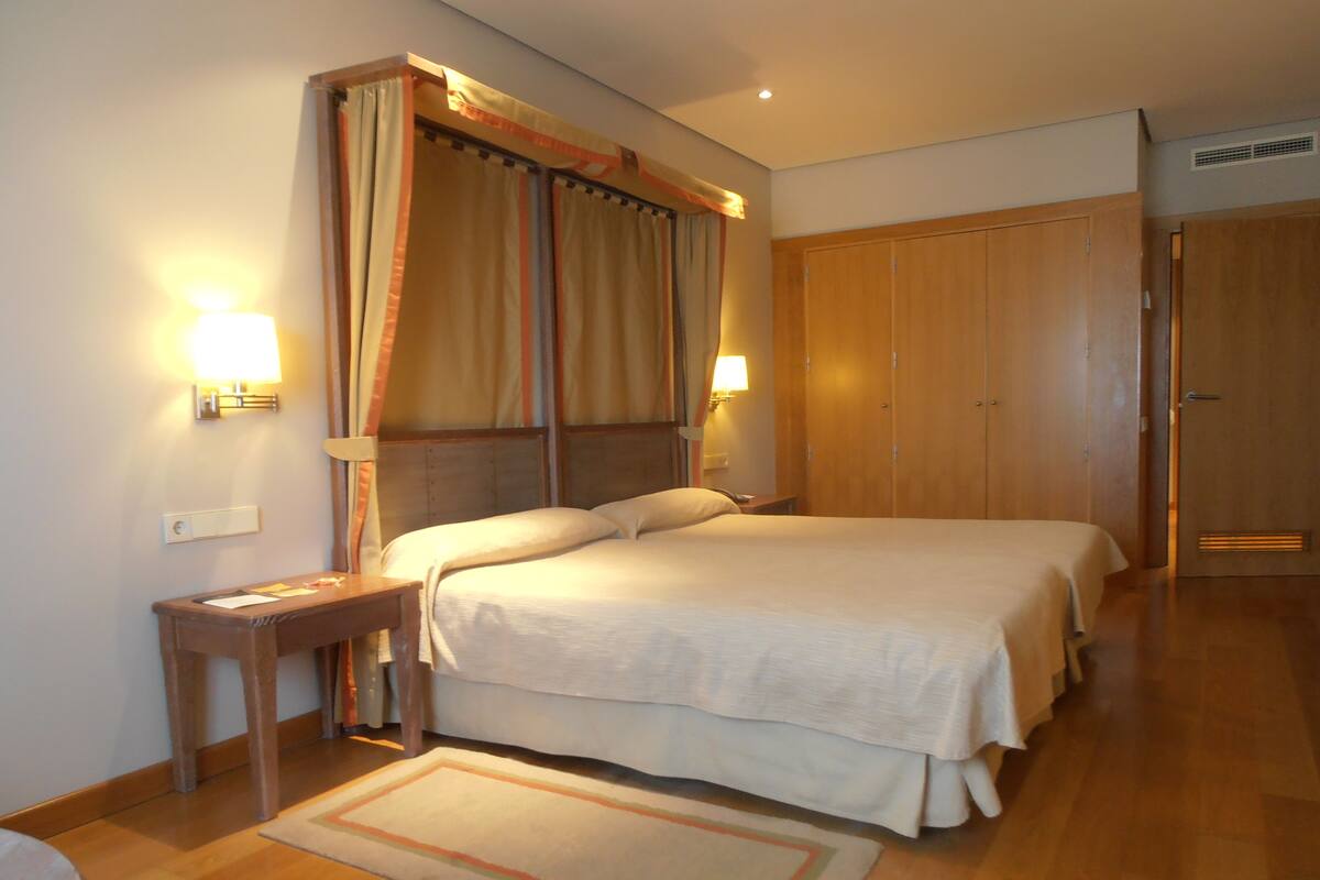 A hotel room with a large bed, a nightstand, a desk, and a wardrobe.