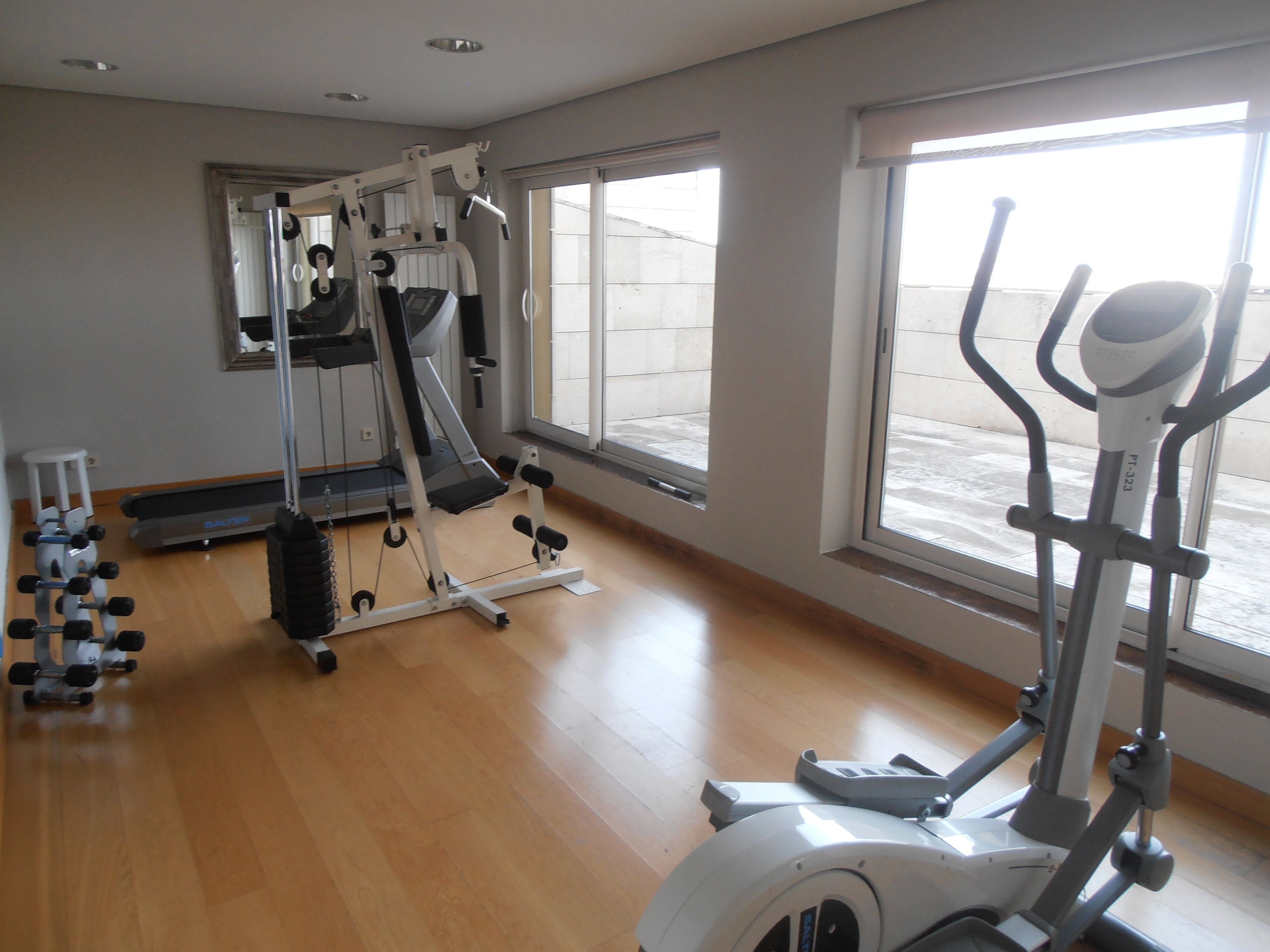 A gym with exercise equipment, large windows, and wooden flooring.