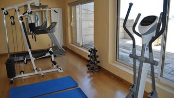 Een sportschool met trainingsapparatuur, een loopband en een raam met uitzicht op buiten.