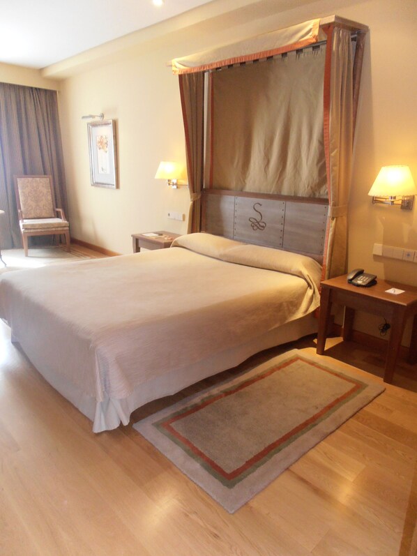 A spacious hotel room with a large bed, a chair, a bedside table with a lamp, and a nightstand with a phone.