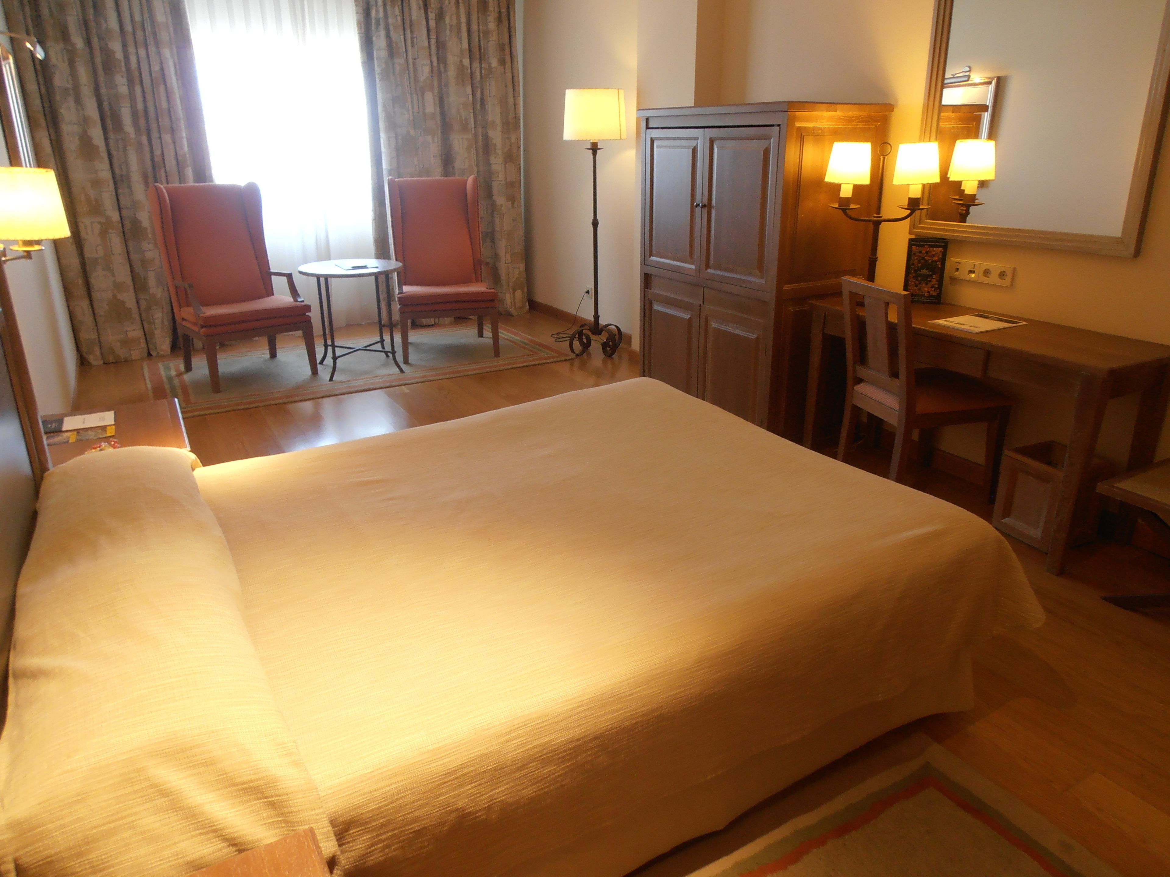 A hotel room with a large bed, two armchairs, a desk, and a wardrobe.