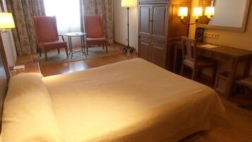 A hotel room with a large bed, two armchairs, a desk, and a wardrobe.
