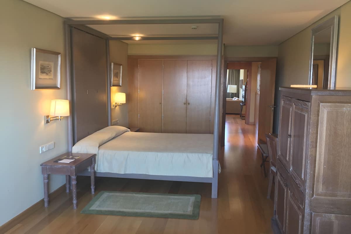 A bedroom with a four-poster bed, wooden wardrobe, and a small bedside table with a lamp.