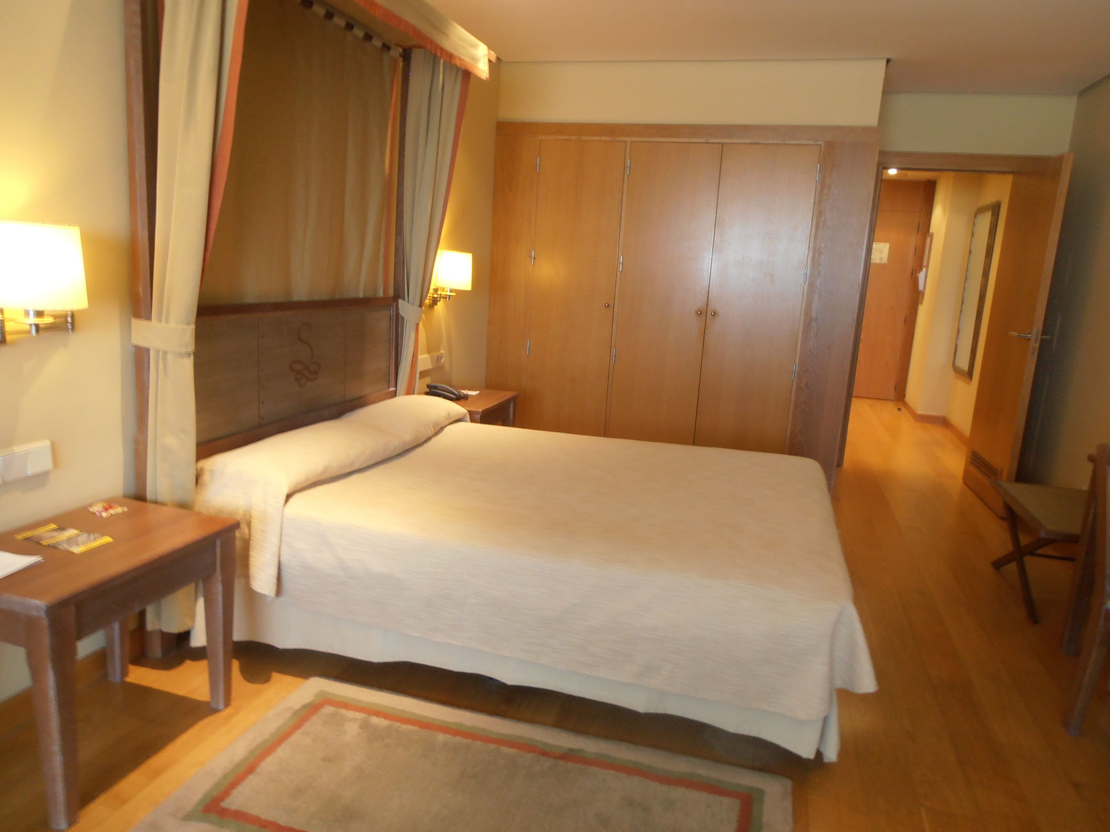 Habitación de hotel con una cama grande, una mesita de noche, una lámpara y un armario.