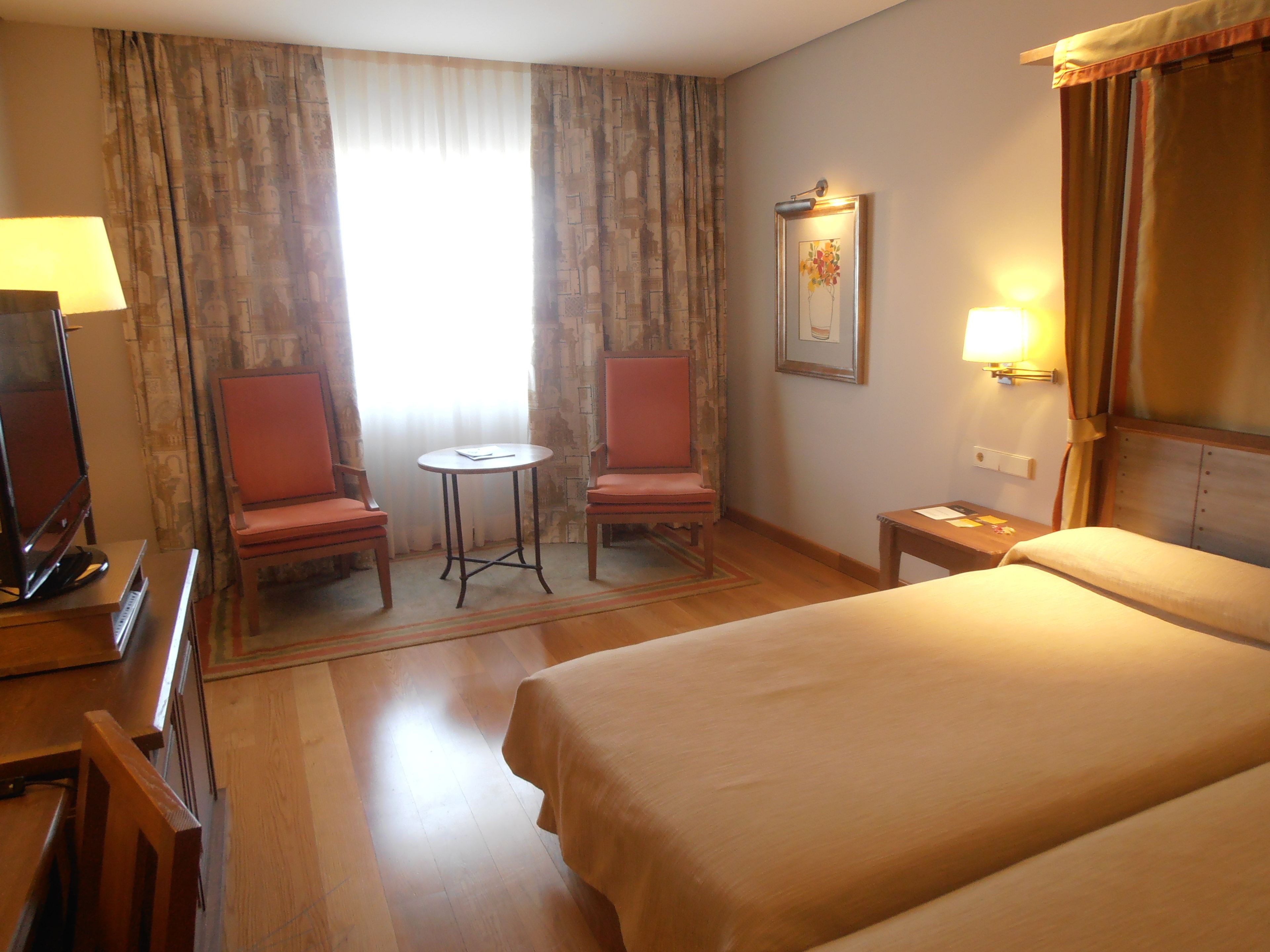 Une chambre d’hôtel avec un lit, deux chaises, une petite table, un téléviseur et un tableau au mur.