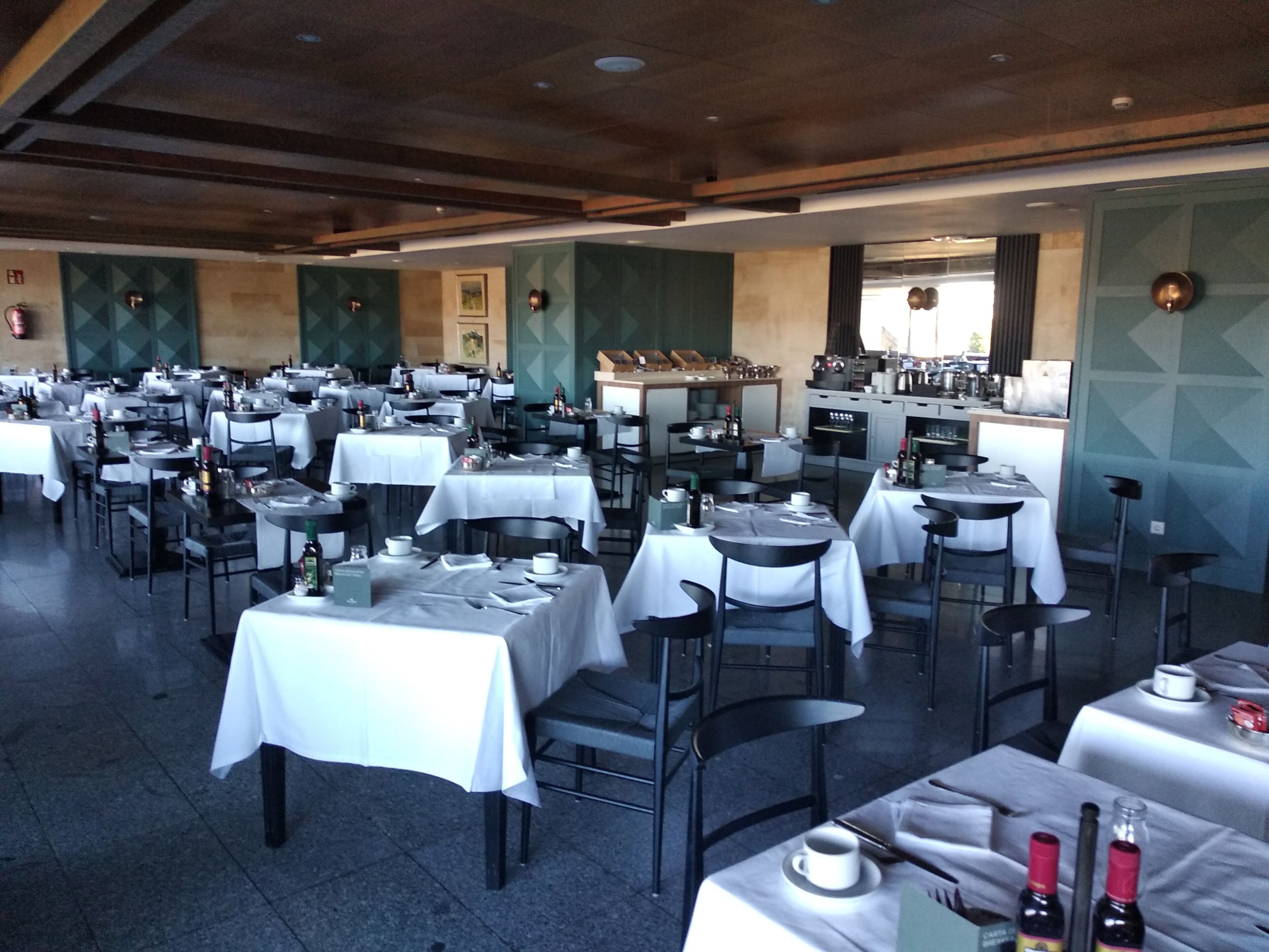Un restaurante amplio con varias mesas y sillas, una zona de bar y vistas a la ciudad.