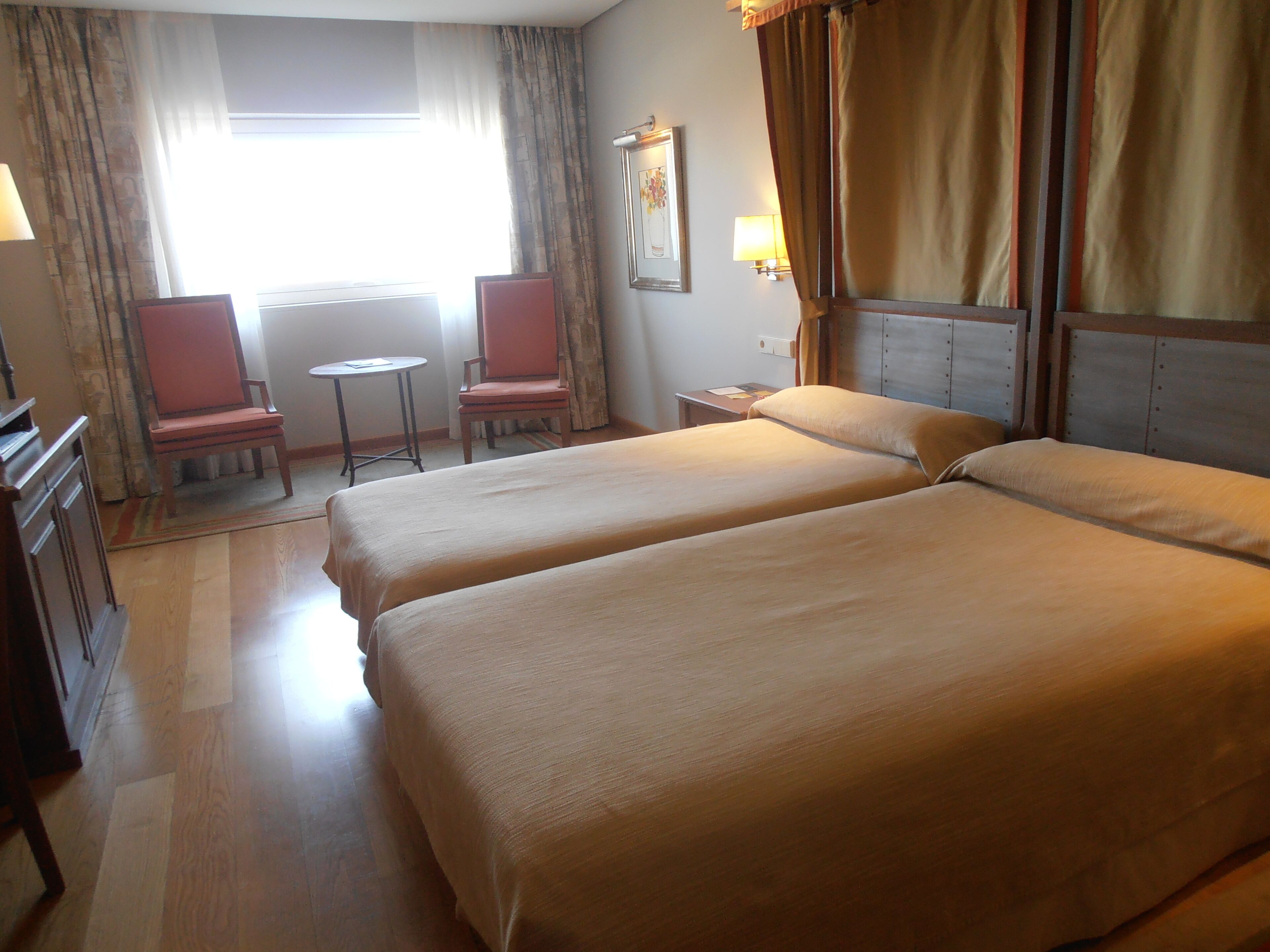Habitación de hotel con dos camas, un escritorio, una silla, una mesita y cortinas.