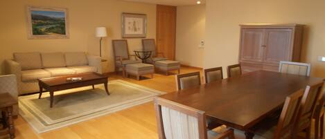 A spacious living room with a wooden dining table, comfortable seating, and a large window.