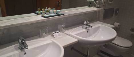 A bathroom with two sinks, a toilet, and a mirror. There are toiletries on the counter.