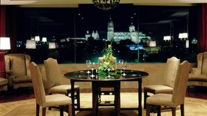A dining area with a round table, four chairs, a chandelier, and a view of a cityscape at night.
