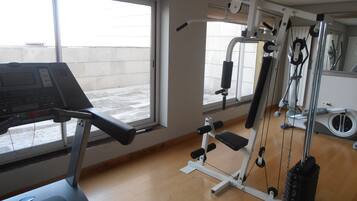 Un gimnasio con cinta de correr, máquinas de pesas y un espejo.