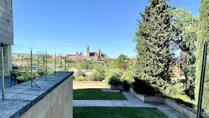 A rooftop terrace with a view of a historic building in the distance, a well-maintained lawn, and a stone wall.