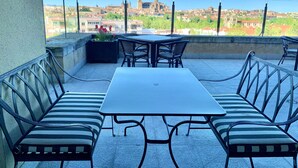A rooftop terrace with a table and chairs, a planter with flowers, and a view of a cityscape including a prominent tower.