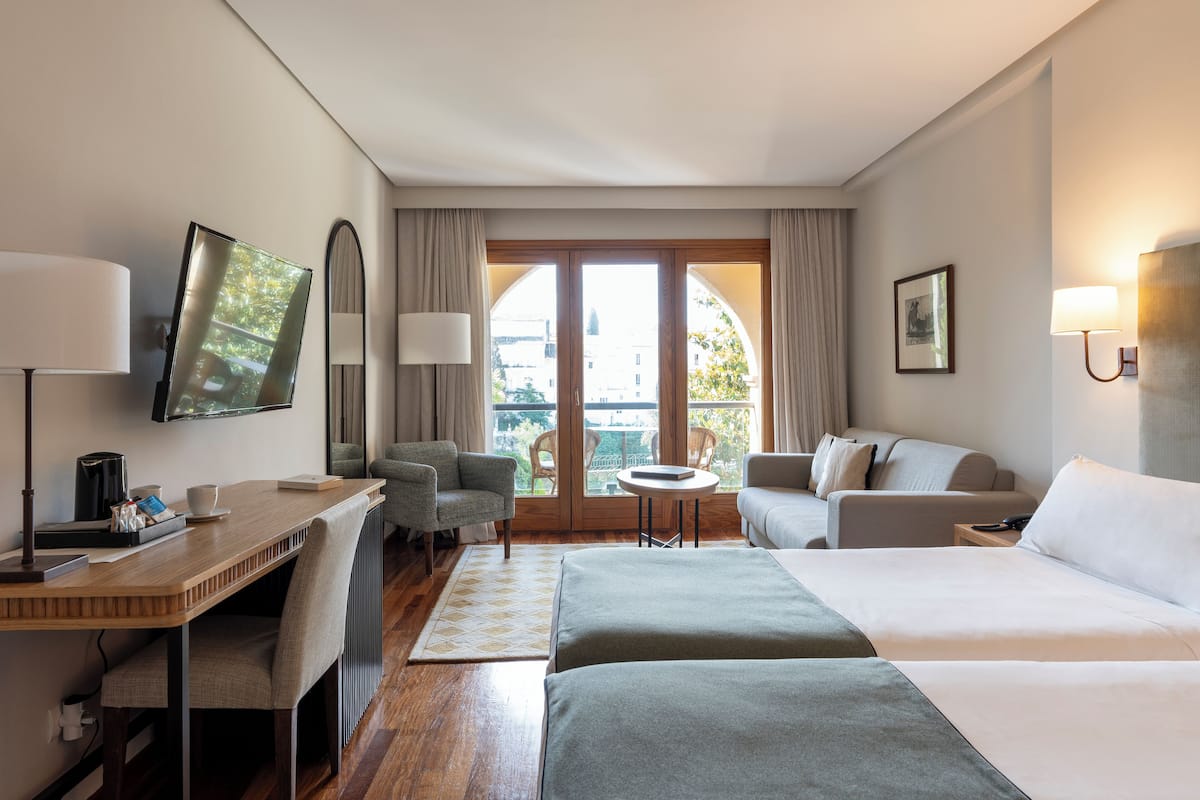 A hotel room with a bed, a desk, a chair, a sofa, and a balcony with a view.