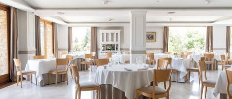 A spacious dining area with multiple round tables, each set with white tablecloths and wooden chairs.