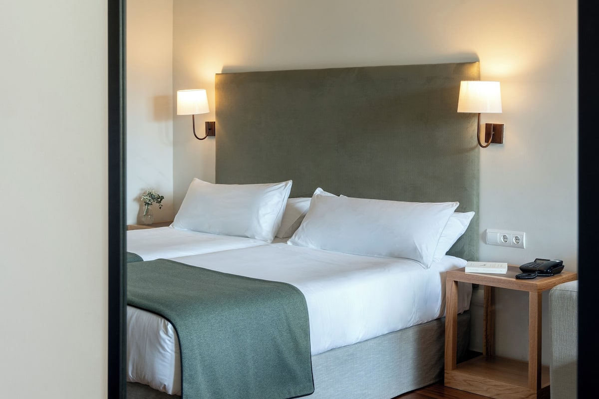 A hotel room with a bed, bedside lamps, a nightstand, and a wooden floor.