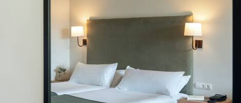 A hotel room with a bed, bedside lamps, a nightstand, and a wooden floor.
