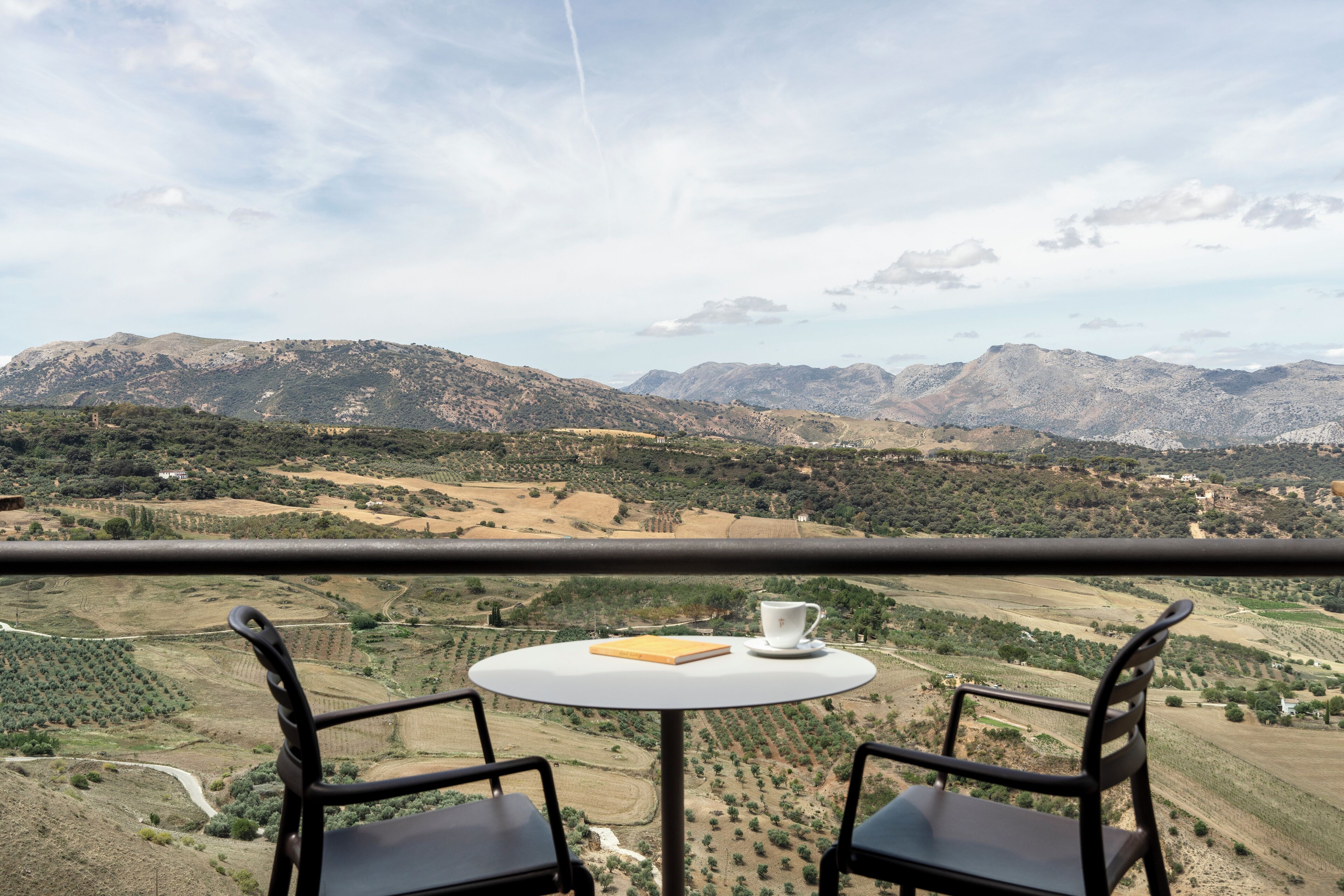 A balcony with a table and two chairs, overlooking a mountainous landscape.