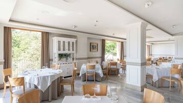Un comedor espacioso con varias mesas redondas, sillas de madera y vistas al exterior.