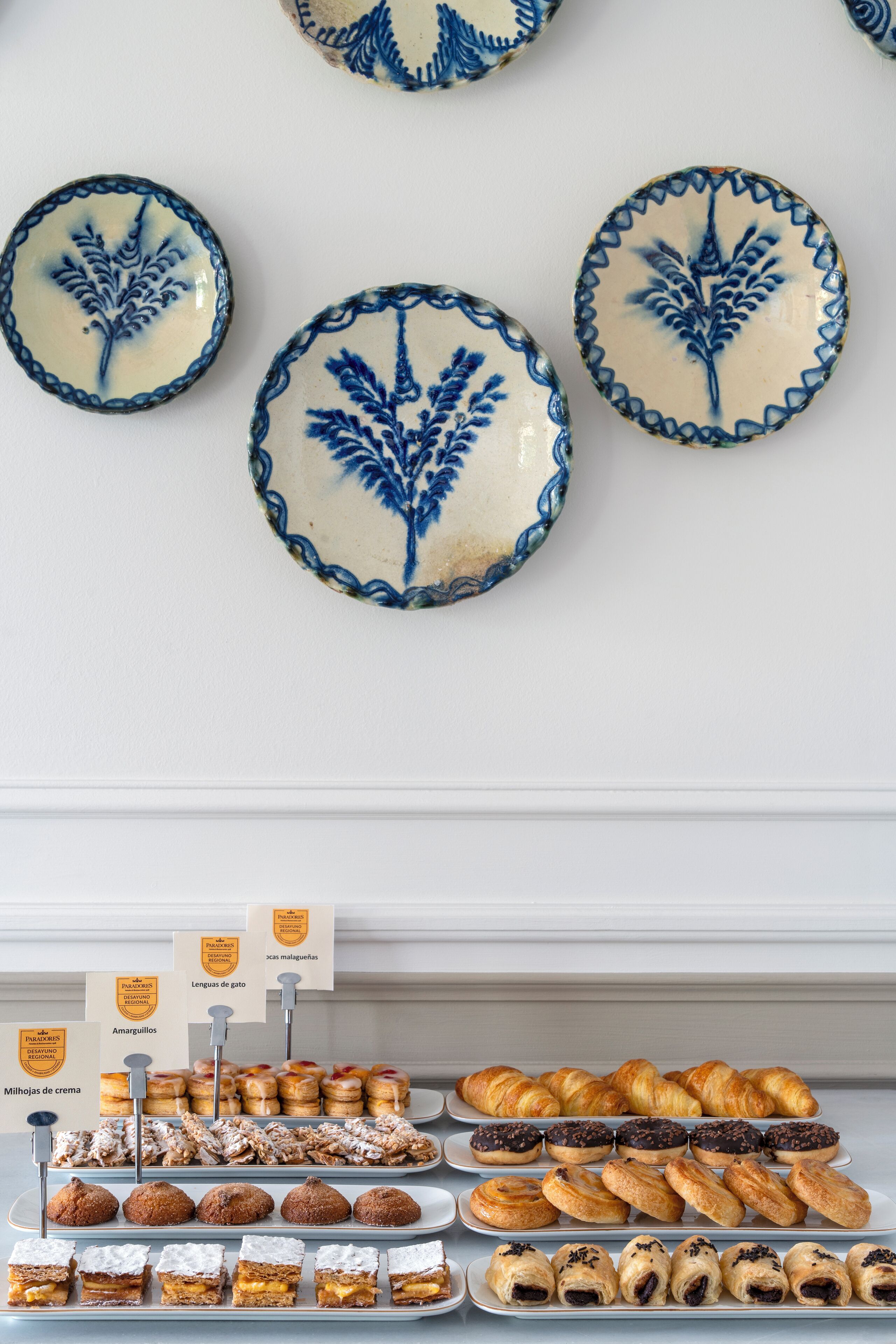Una vitrina de pastelería con dulces y una pared decorada con platos de cerámica.