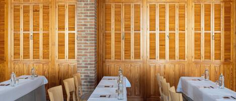 A dining area with wooden panel walls, tables set with white tablecloths, and chairs.
