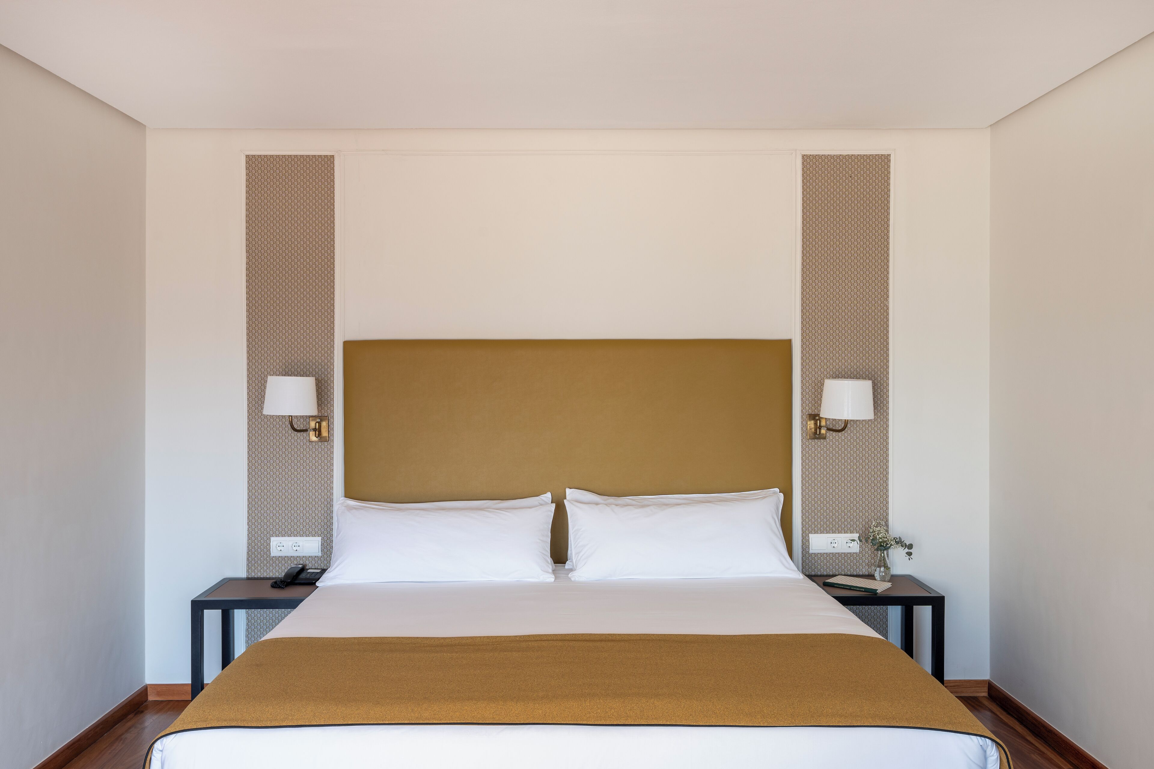 A hotel room with a large bed, two bedside tables, and two wall-mounted lamps.