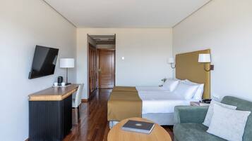 Una habitación de hotel con cama, sofá verde, mesa de centro de madera, escritorio con televisor y lámpara de noche.