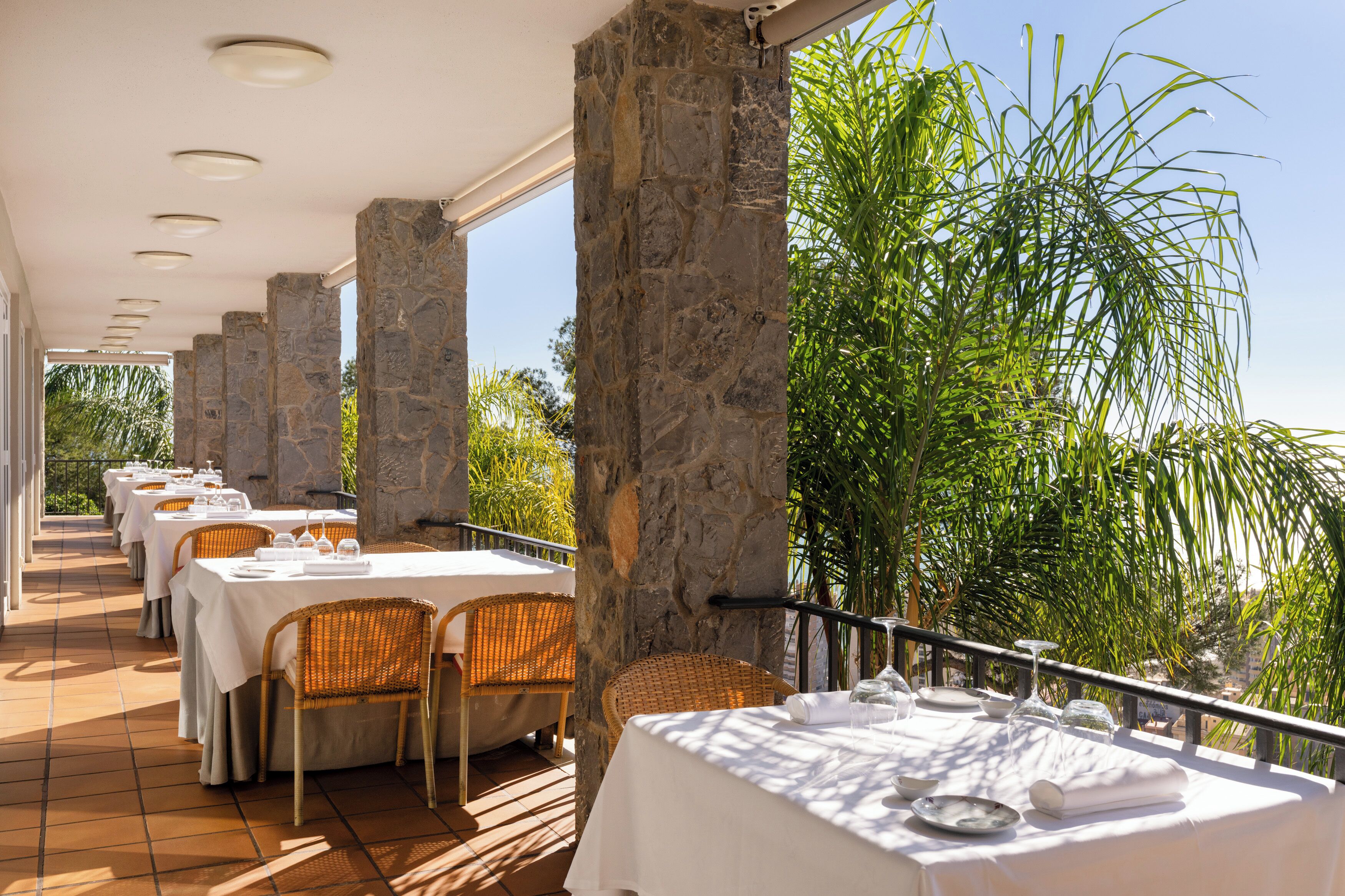 Un restaurante con pilares de piedra, manteles blancos y sillas de mimbre.