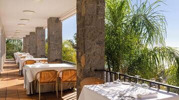Un restaurante con pilares de piedra, manteles blancos y sillas de mimbre.