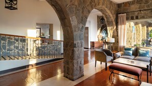 A spacious lobby with stone arches, a wooden staircase, and a seating area with a sofa and table. - Parador de Malaga Gibralfaro  (Málaga)