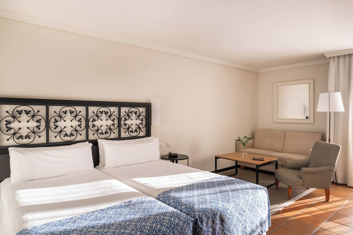A hotel room with two beds, a sofa, a small table, and a lamp.