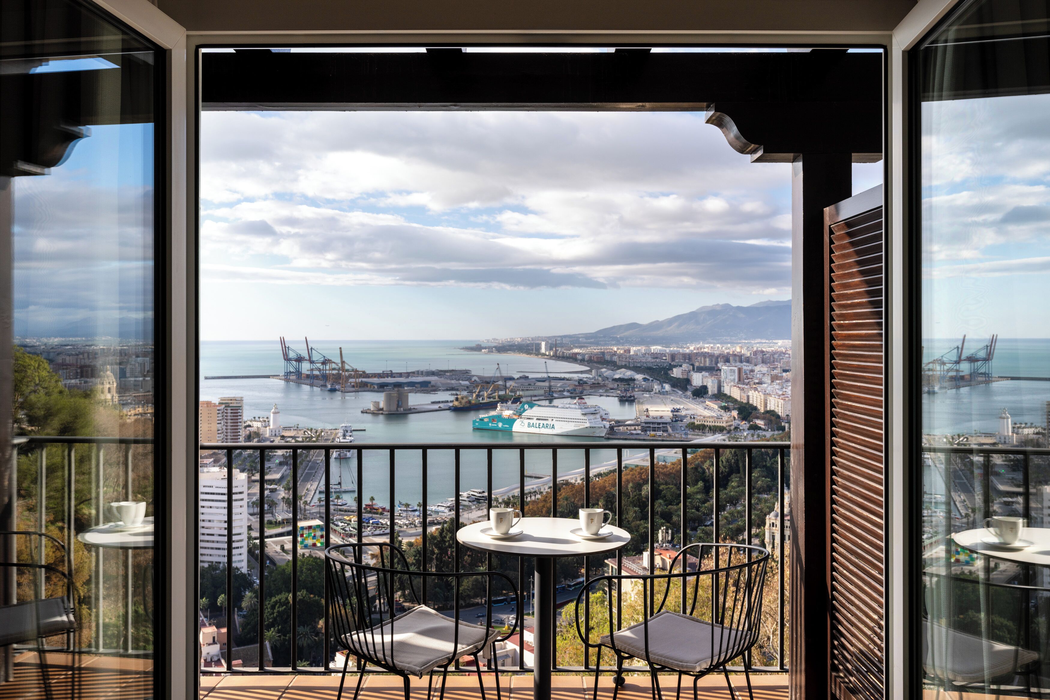 A balcony with a table and chairs overlooking a cityscape with a bridge and port.