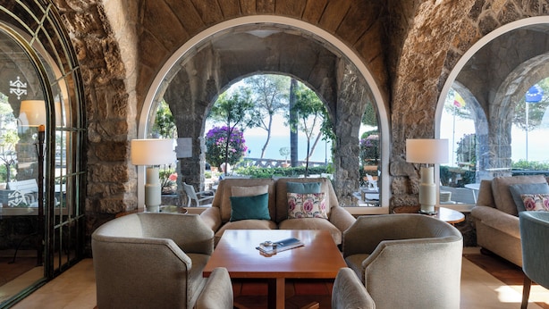 A cozy seating area with a stone archway, a wooden table, and two lamps. - Parador de Malaga Gibralfaro  (Málaga)