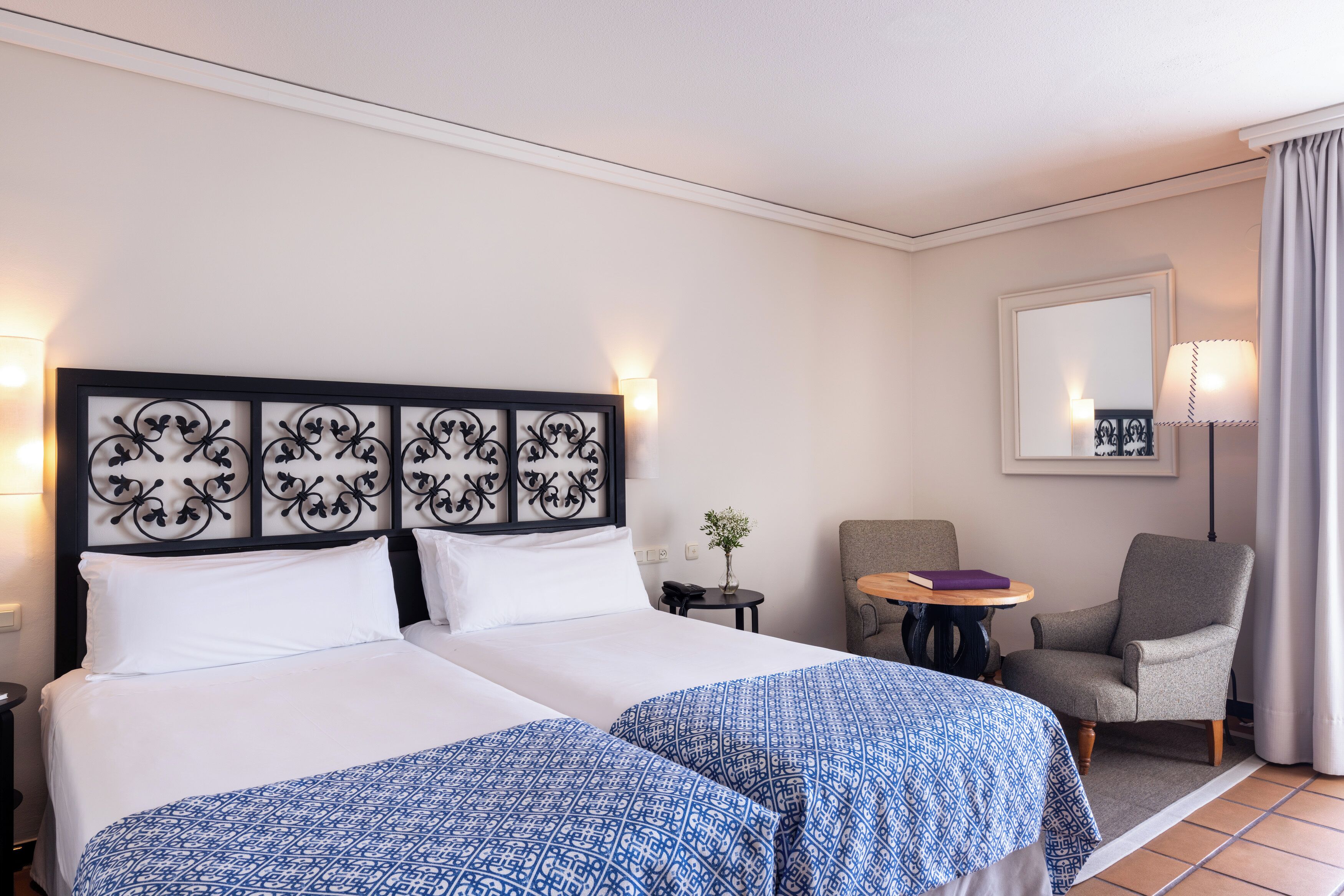 Habitación de hotel con dos camas, un escritorio, una silla, una lámpara y un espejo.