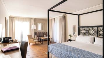 Ein Hotelzimmer mit Himmelbett, Schreibtisch mit Lampe, Stuhl, Sofa und Fernseher.