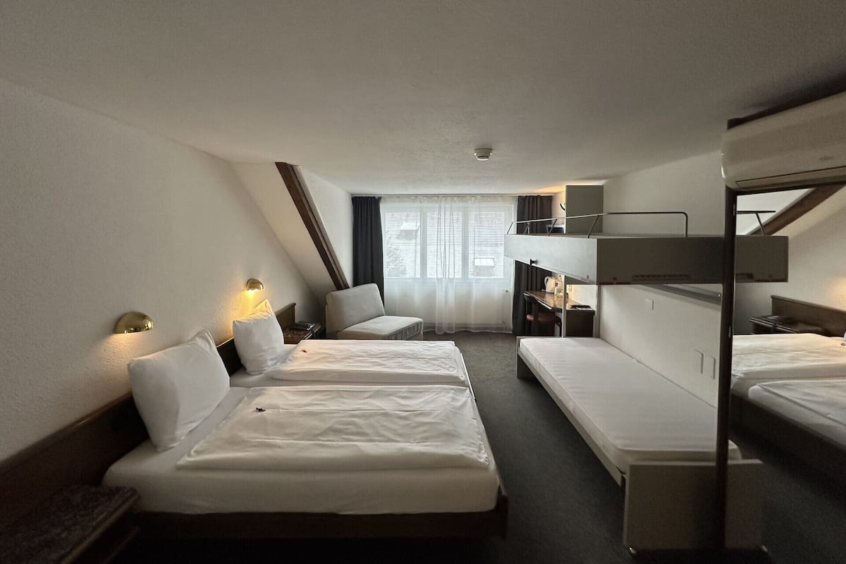 A hotel room with two beds, a desk, a chair, and a bunk bed.