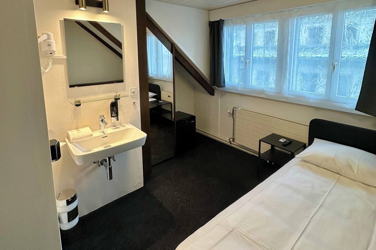 A hotel room with a bed, a sink, a mirror, a window, and a staircase.