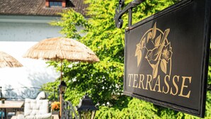 A terrace with a sign reading "TERRASSE," outdoor seating, and a view of a building with a thatched roof. - BASLERTOR Summer Pool Hotel (Lucerne)