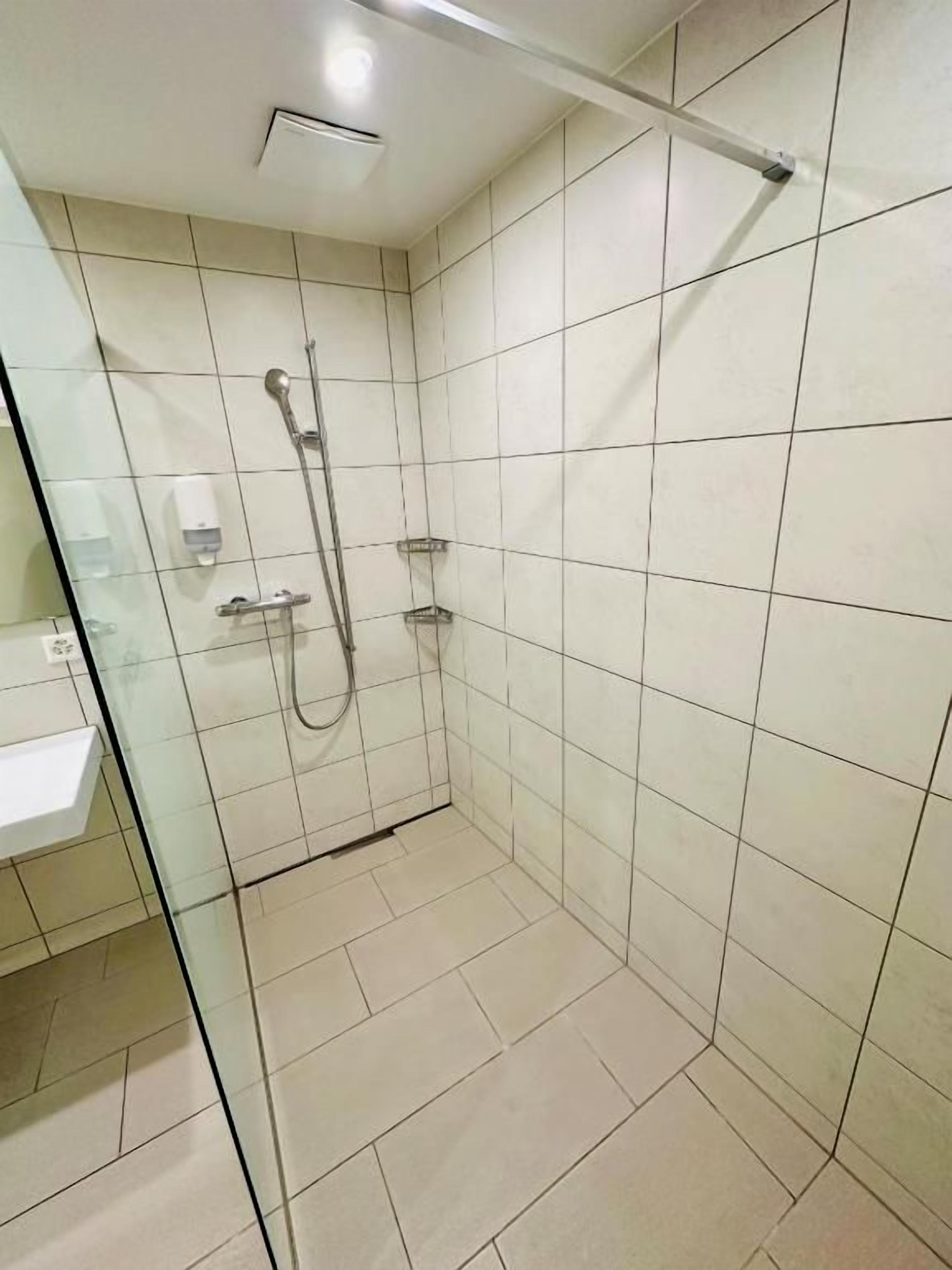 A small, tiled bathroom with a glass partition, a shower, and a hand dryer.