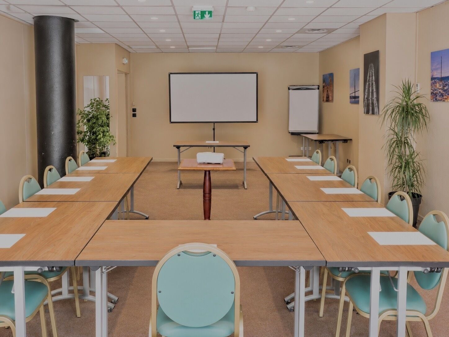 Ein Konferenzraum mit einem langen Tisch, Stühlen, einem Projektor, einer Tafel und einer Pflanze.