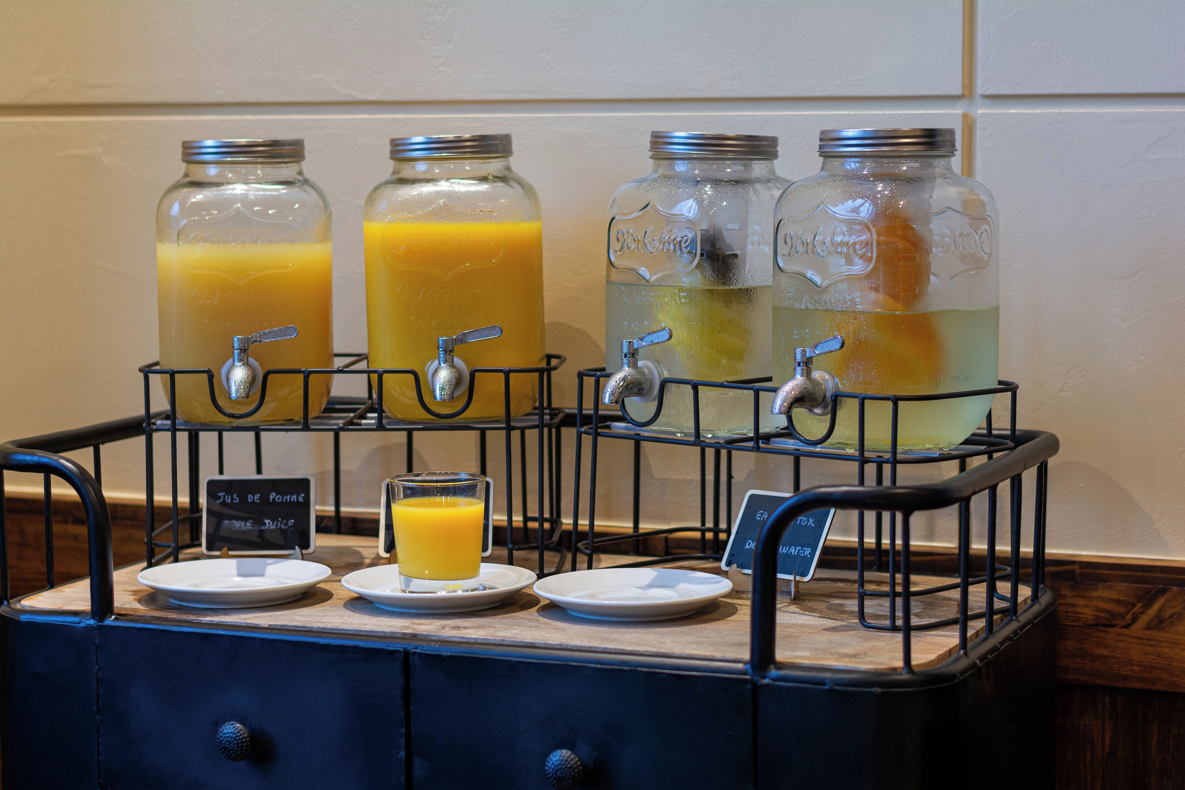 A beverage dispenser with multiple taps and glasses, including a sign indicating juice and water options.