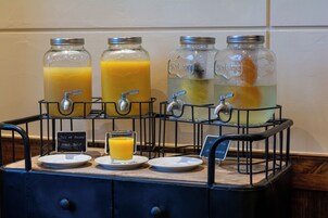 Dispensador de bebidas con varios grifos y vasos, incluyendo un cartel que indica opciones de jugo y agua.