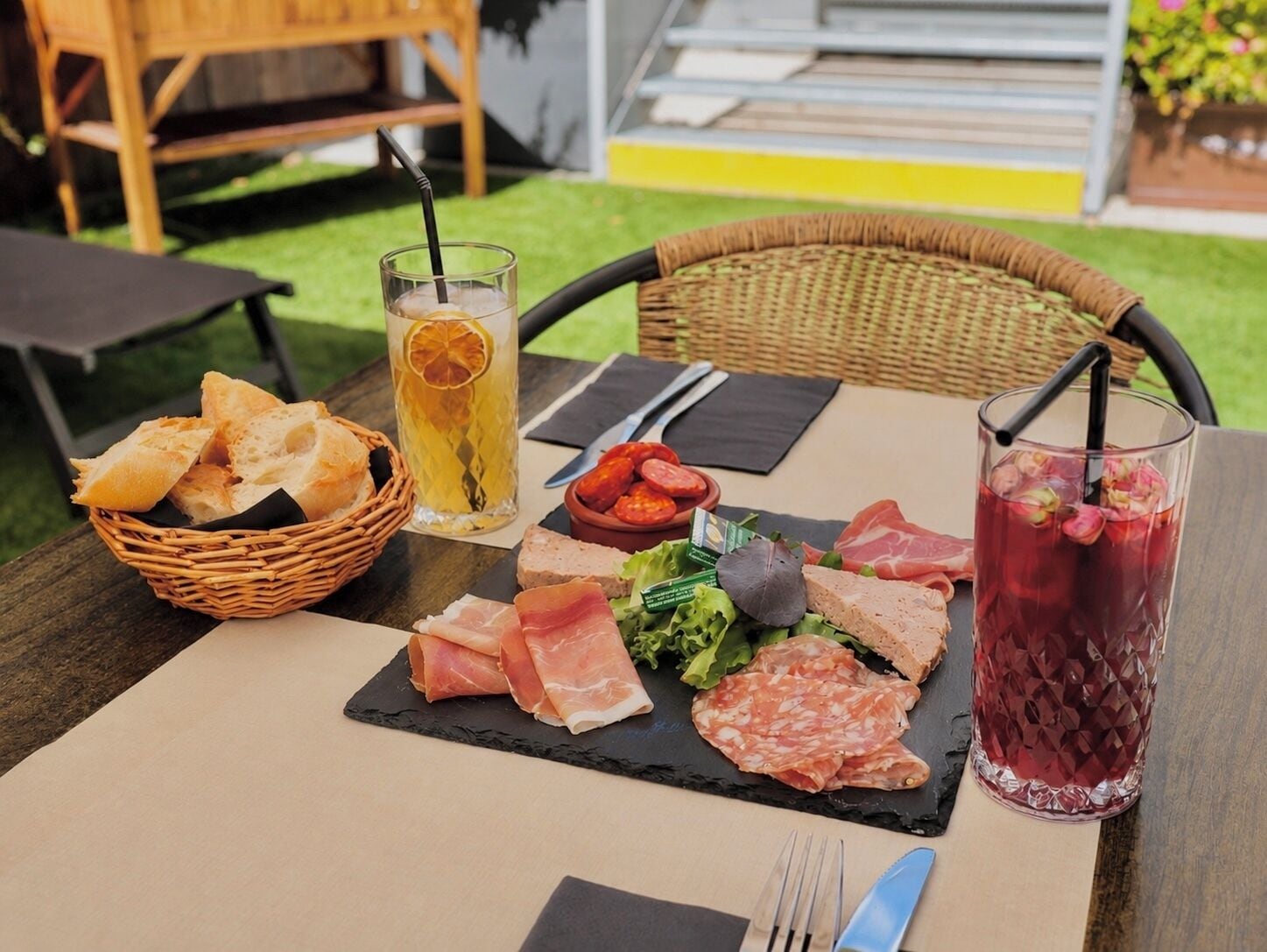 A table set with a variety of meats, a glass of iced beverage, and a basket of bread.