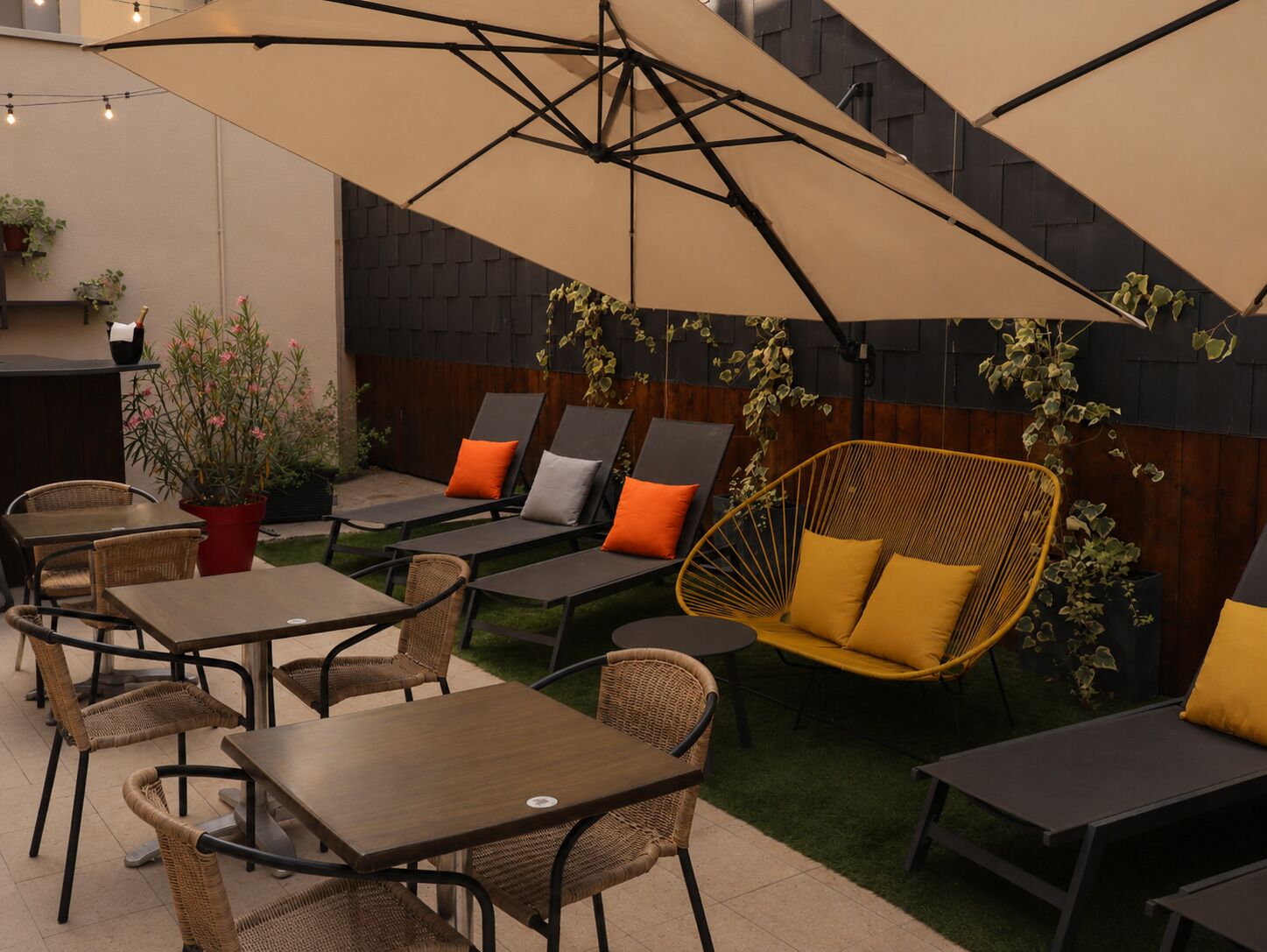 An outdoor seating area with tables and chairs, a hanging chair, and a large umbrella providing shade.