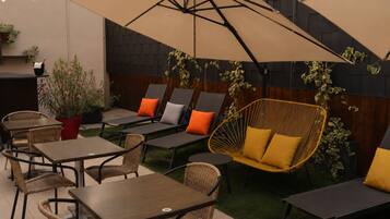 An outdoor seating area with tables and chairs, a hanging chair, and a large umbrella providing shade.