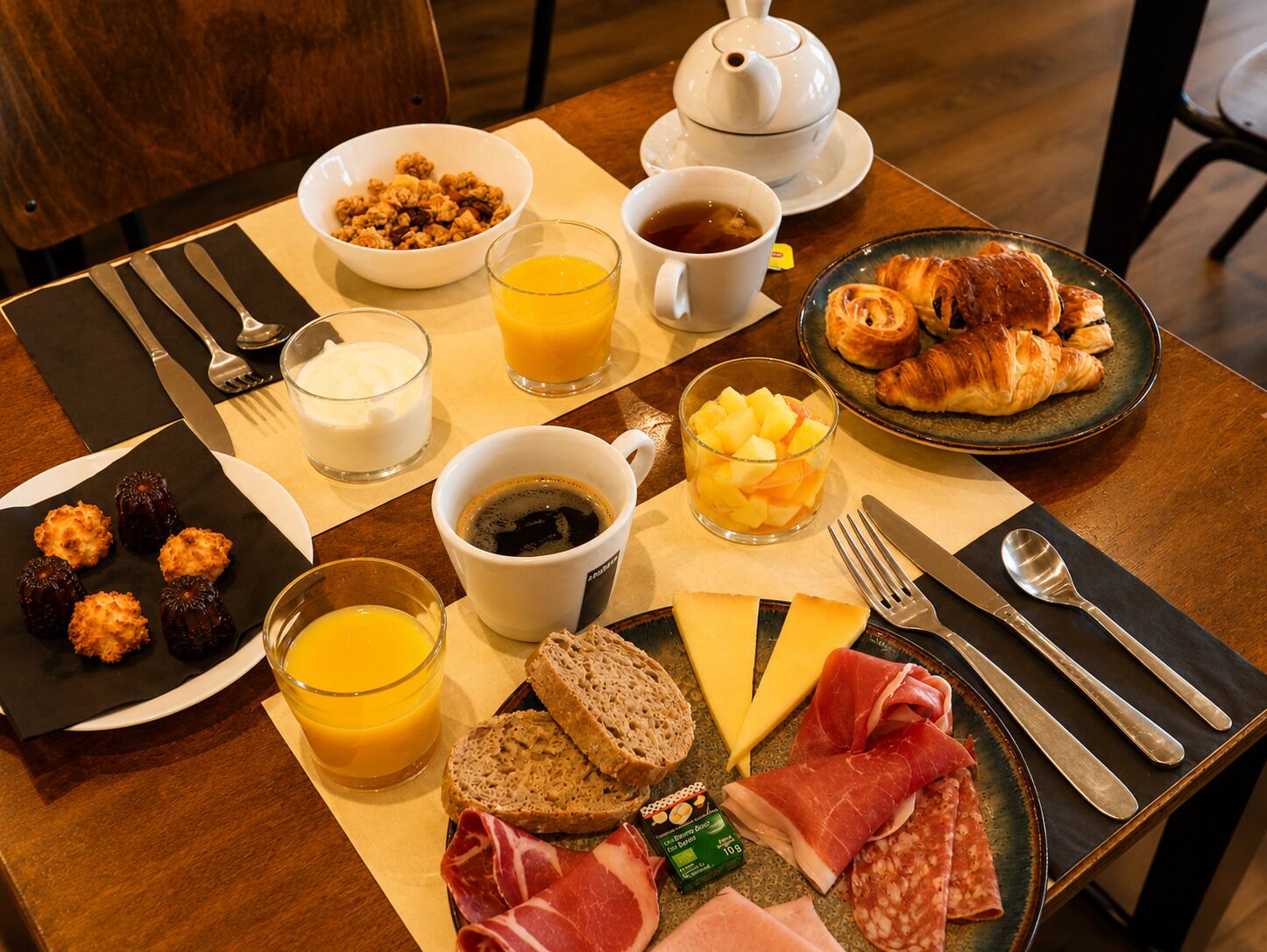 A breakfast setting with croissants, fruit, cheese, and meats on a table.
