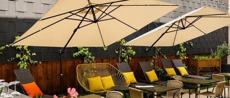 An outdoor seating area with tables and chairs, umbrellas, and plants.