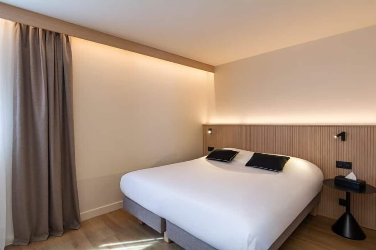Een hotelkamer met een bed, gordijnen, een nachtkastje en een wandlamp.