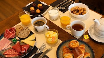 A breakfast table with various food items, including meats, cheese, croissants, and fruit.